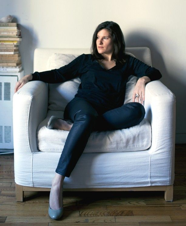 Adèle Jancovici seated in a white armchair beside a stack of books